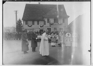 Primizfeier Ruf-Eisele in Sigmaringendorf 1936; Im Mittelpunkt Neupriester mit Eltern, dabei Geistlichkeit; im Hintergrund Zuschauer vor dem Haus Bäckerei-Konditorei Josef Aleker