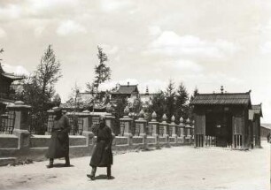 Ulan Bator. Mongolisches Ehepaar am Gandan-Kloster (1801/1850). Ansicht mit Umfassungsmauer und Holzbauten mit Gebetsmühlen