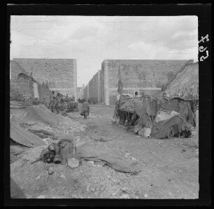Allaines (Dep. Somme, Frankreich): von hohen Mauern festungsartiger Gebäude gesäumter Weg, davor ein Lagerplatz ("Kanal") [trocken gelegter Canal du Nord?]