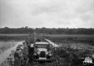 Überfahrt mit dem Auto : Ein Automobil der Expedition überquert eine Landbrücke auf einer provisorisch errichteten Brücke aus Baumstämmen.