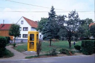 Dorfplatz mit Spielgeräten auf Grünfläche; Telefonzelle