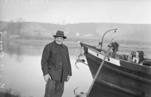 Elbschiffer, ein alter Schiffer im Ruhestand an der Elbe, neben ihm ein Schleppkahn