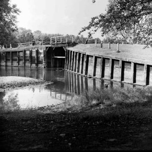 Alster: Wulksfelder Schleuse mit Schleusenbrücke: vorn Böschung: in der Mitte rechts und links Holzverschalungen: hinten links am Geländer Mann: dahinter Bäume