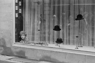 Schaufenster eines Hutgeschäfts mit sich in der Scheibe spiegelnden Passanten