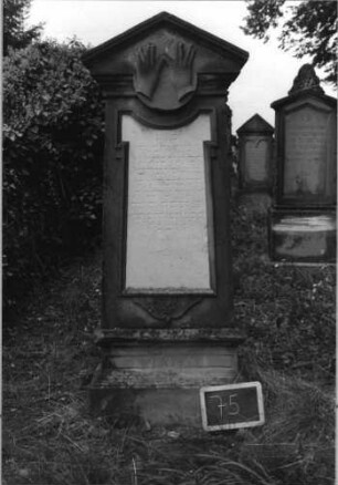 Grabstein 75 (Index: 100080587) Material: Sandstein, weiße Marmorplatte Zustand: Sockel, verwittert mit Textverlust Maße HxBxT: 165x48x20 cm Beschreibung: kon. Stele, getreppt. Sockel, giebelart. Abschl. m. Verdach. , Schriftplatte:Sonderform Symbolik: segnende Hände: Grabstein 75