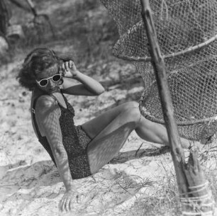 Frau im Bikini mit Sonnenbrille neben einer Reuse am Strand