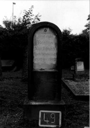Grabstein 49 (Index: 100110251) Material: Sandstein mit weißer Marmorplatte Zustand: leicht verwittert Maße HxBxT: 124x40x19 cm Beschreibung: Stele, Sockel, Rundbogenabschluß Symbolik: sechszackiges Sternchen: Grabstein 49