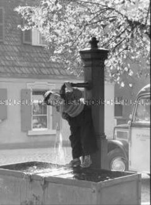 Kind trinkt an einem Brunnen
