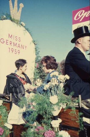 Reinfeld: Karpfenfest: Umzug: Paul-von-Schoenaich-Straße: Festwagen der Opal-Strumpffabrik Margaritoff & Schaffer mit Blumenschmuck: Miss Germany 1959 Carmela Künzel auf Thron, mit Gefolge: rechts Kutscher und Firmenschild: 11. Oktober 1959