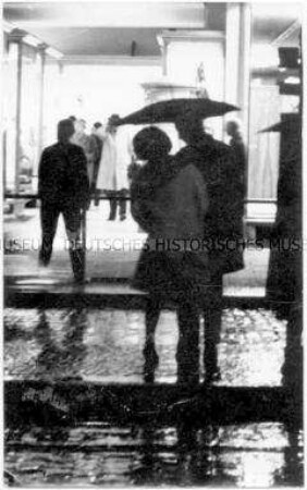 Paar unter einem Regenschirm, im Hintergrund weitere Menschen