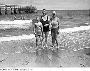 Strandleben. Vater mit 2 Töchtern (alle in Badekleidung) für Fotografen posierend; im Hintergrund die Seebrücke