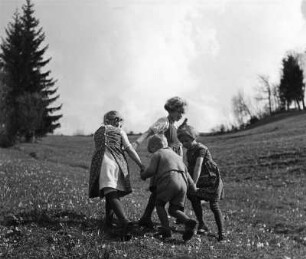 Kinderbilder. Vier Kinder beim Ringelreihen auf einer Wiese