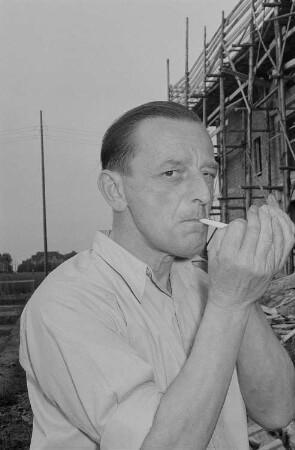 Eine Person vor einer Baustelle beim Entzünden einer Zigarette