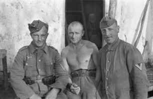 Zweiter Weltkrieg. Zur Einquartierung. Sowjetunion. Drei Angehörige der deutschen Wehrmacht vor einer Bauernhütte