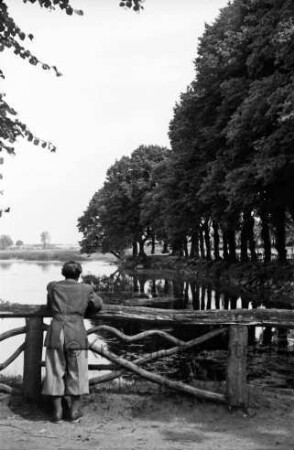 Mühlenteich: vorn links am Holzgeländer Mann: rechts Baumreihe: dazwischen Tische und Stühle der Gaststätte "Glinder Mühle": hinten links Wiesen
