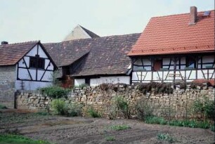 bewachsene Trockenmauer, dahinter Wohnhaus und Wirtschaftsgebäude