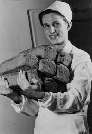 Werbung für die "Pro" Bäckerei. Junger Bäcker hält mehrere Brote auf dem Arm.
