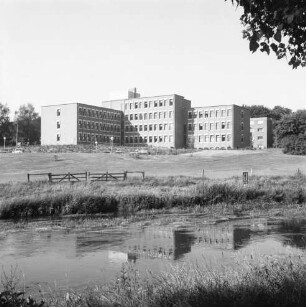 Trave: am gegenüberliegenden Ufer Wiesen, Zaun und Holzgatter: dahinter Kreiswehrersatzamt am Berliner Ring: hinten Bäume