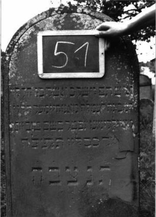 Grabstein 51 (Index: 100103625) Material: Sandstein Zustand: stellenweise leicht verwittert, am Rand abblätternd Maße HxBxT: 136x51x7 cm Beschreibung: Stele, Rundbogenabschluss, Schriftfeld eingetieft, im Bogen eingeritzte Levitenkanne Symbolik: Levitenkanne: Grabstein 51 (Detailaufnahme)