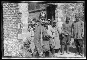 Lille (Dep. Nord, Frankreich): Wachsoldat mit Pickelhaube vor einem Mauertor, im Hintergrund Gefangene (Nahaufnahme) ("Einbringen von Gefangenen auf der Zitadelle Lille")