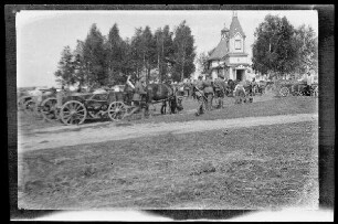Mehrere Fuhrgespanne und Soldaten vor einer kleinen Holzkirche