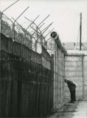 Älterer Mann späht von West-Berlin aus durch die Mauer nach Ost-Berlin