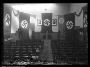 Geschmückter Festsaal mit Adolf-Hitler-Büste und Hakenkreuzfahnen