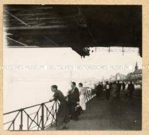 Menschen stehen unter einer Brücke am Rheinufer Köln