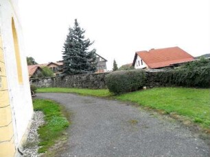 Kirchhof im Osten mit Kirchhofmauer (Wehrgang mit Schießscharten abgetragen) in übersichtlichem Verlauf (teils stark überwachsen)