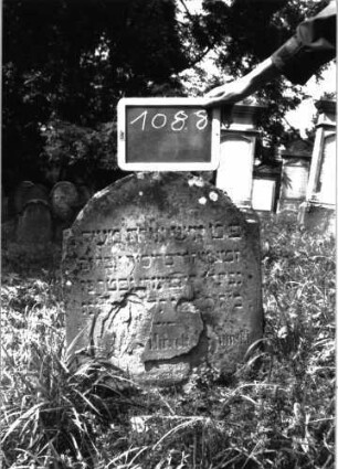 Grabstein 1088 (Index: 100104139) Material: Sandstein Zustand: stark verwittert Maße HxBxT: 57x47x13 cm Beschreibung: Stele mit eingezogenem Rundbogenabschluss: Grabstein 1088