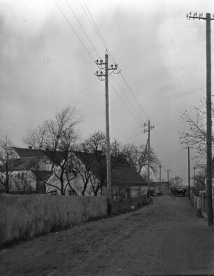 Sachsen? Erste 110 kV-Freileitung des Elektroarmaturenwerks Radebeul-Kötzschenbroda. Dorfstraße mit Leitungsmasten. Blick gegen Gehöft mit Einfriedung