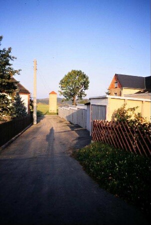 Dorfstraße mit Gärten, hinten Trafohäuschen