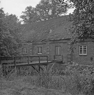 Denkmal: Kupfermühle mit beschädigtem Dach und in desolatem Zustand: vorn links beschädigte Holzbrücke über Glinder Au: davor Sträucher: hinten Bäume