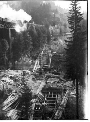 Verschalungen der zur Gründung der Pfeiler gegrabenen Schächte und alter Viadukt mit einem darauf befindlichen Eisenbahnzug