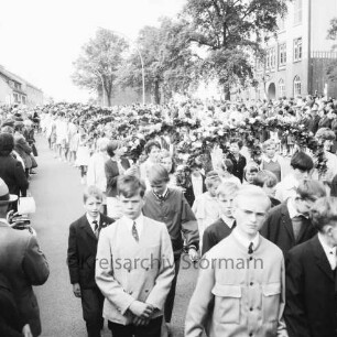 Kindervogelschießen: Umzug: Hamburger Straße: vorne Jungen, dahinter Mädchen mit Blumenbögen: rechts Theodor-Mommsen-Schule: an den Straßenrändern Zuschauer: vorne links Fotograf, 7. Juni 1968