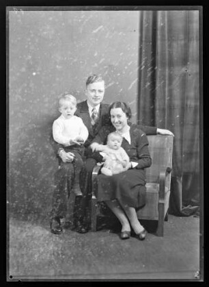 Portraitaufnahme Vater, Mutter und zwei kleine Kinder, eines bei der Mutter auf Schoß sitzend