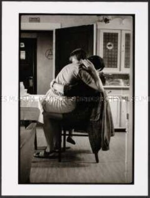 Sich umarmendes Paar auf dem Küchenstuhl (Sonderthema: Liebe)