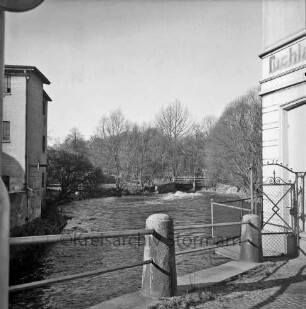 Trave: Blick von Lübecker Torbrücke auf Stauwehr: links Gewerbegebäude: im Vordergrund Geländer, rechts Hausecke, Gittertor