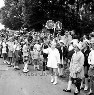 Kindervogelschießen: Festumzug: Klassen mit Blumenbögen: Schulkinder in Kostümen: dahinter Zuschauer: in der Mitte Verkehrsschild: hinten Bäume