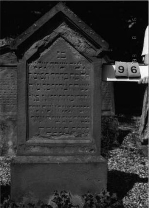 Grabstein 96 (Index: 100086580) Material: Sandstein Zustand: stark abgeblättert Maße HxBxT: 151x60x18 cm Beschreibung: Stele, Sockel, giebelartiger Abschluß mit Verdachung: Grabstein 96