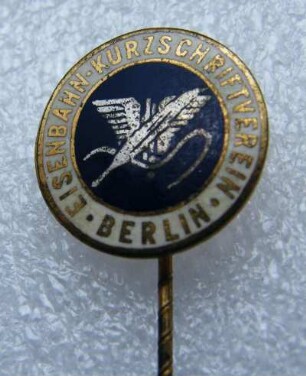 Mitgliedsabzeichen Eisenbahn-Kurzschriftverein Berlin (mit langer Nadel) : Sammlung Beinhorn. Mitgliedsabzeichen Eisenbahn-Kurzschriftverein Berlin (geflügelte Feder und in Kurzschrift "Einheit" auf blauem Grund, mit langer Nadel). Email, Metall; Durchmesser 17 mm (nach 1924). Dresden: SLUB R c 0261