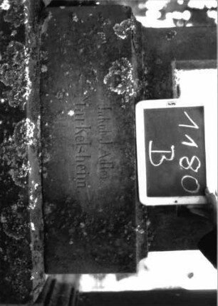 Grabstein 1180 (Index: 100104324) Material: Sandstein, Marmortafel Zustand: gut erhalten, im Giebel beginnende Verwitterung Maße HxBxT: 198x57x22 cm Beschreibung: Stele auf getrepptem Sockel, giebelartiger, hochgezogener Abschluss mit Eck- und Giebelakroterien (Voluten- u. Blattornamente), eingetieftes, rundbogiges Schriftfeld Symbolik: Blattornamente: Grabstein 1180B