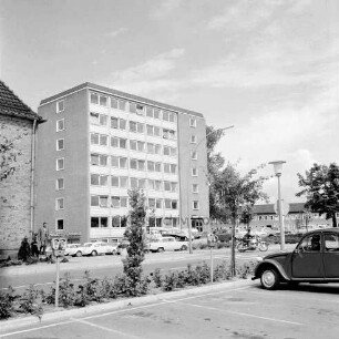 Erweiterungsbau "Hochhaus" [später Gebäude B]: III. Bauabschnitt: Gebäude nach Fertigstellung mit Filiale der Kreissparkasse Stormarn: davor Parkplatz mit Pkws: links Ecke des Finanzamtes und Einmündung Bangertstraße mit Personen: rechts Pkw: hinten Erweiterungsbau II. Bauabschnitt: im Vordergrund Mommsenstraße und Parkplatz am Bahnhof