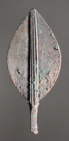 "Blattförmiges Stück eines Gerätes". Lanzettförmige Bekrönung einer geometrischen Nadel (?) mit kannelierter Mittelrippe und je zwei gravierten Delphinen oder Fischen auf beiden Seiten