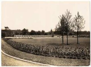 Grünanlage mit Spielplatz, Hindenburg: Grünanlage mit mittiger Rasenfläche, Randbepflanzung, Natursteinmauer und Laubengang sowie Kirche im Hintergrund