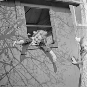 Mädchen mit Zöpfen und Schleife schaut aus einem Spielhaus heraus