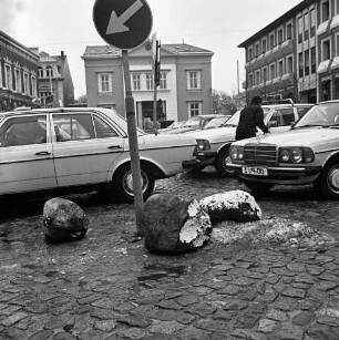 Marktplatz mit parkenden Pkws: vorn Verkehrsschild und beschädigte Findlinge: links zwischen Pkws Mann: hinten Mitte Historisches Rathaus: hinten rechts Stadthaus: hinten links Gebäude der Kreissparkasse Stormarn [Sparkasse Holstein]