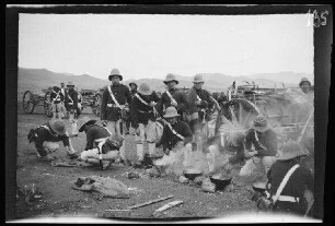Expedition nach Zeluan (=Selouane, Marokko): Soldaten der Artillerie [des spanischen 10. Kavallerie-Regiments "Alcántara" (?)] in hellgestreiften Uniformhosen, dunklen Uniformjacken und Tropenhelmen bei 4 auf kleinen Feuerstellen dampfenden Schüsseln ("beim Abkochen")