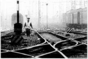 Ein Arbeiter läuft entlang vieler Eisenbahngleise (Altersgruppe 14-17)