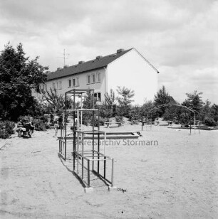 Kellerberg-Süd: Kinderspielplatz in Neubaugebiet: vorn und hinten rechts Klettergerüste: hinten links drei Kinder auf Bank und zwei Kinder in Sandkasten: hinten rechts weiterer Sandkasten und Bänke: dahinter Büsche: hinten Wohnblock